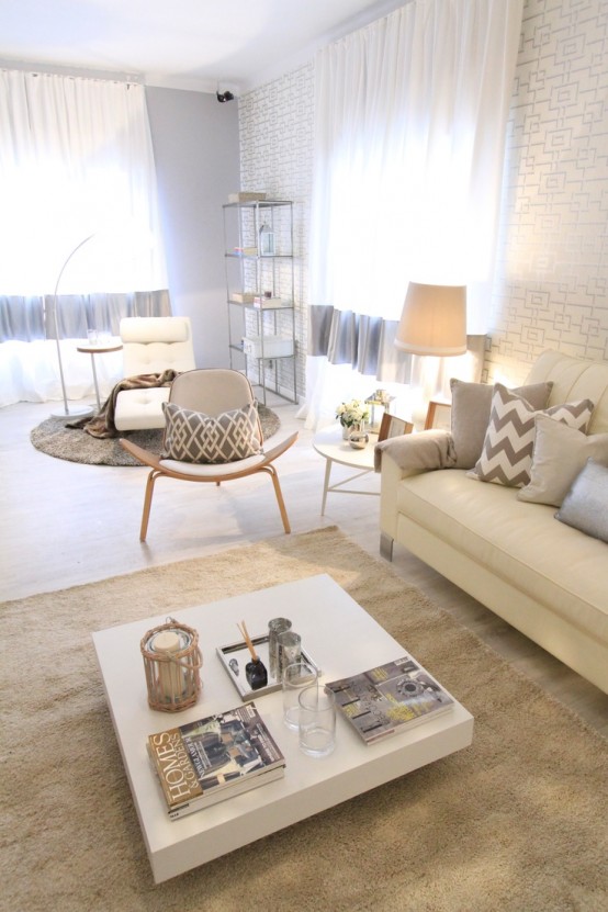 a modern neutral living room with an accent wall, a creamy sofa, a lounger, a grey chair, a low white coffee table and a shelving unit