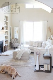 a neutral farmhouse living room with a built-in fireplace and shelves, a creamy sectional, a pouf, a reclaimed wooden shelf and some cozy decor