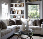 a cozy modern neutral living room with French windows, built-in shelves, a sectional and mismatching pillows, a glass coffee table and shiny metallic accents