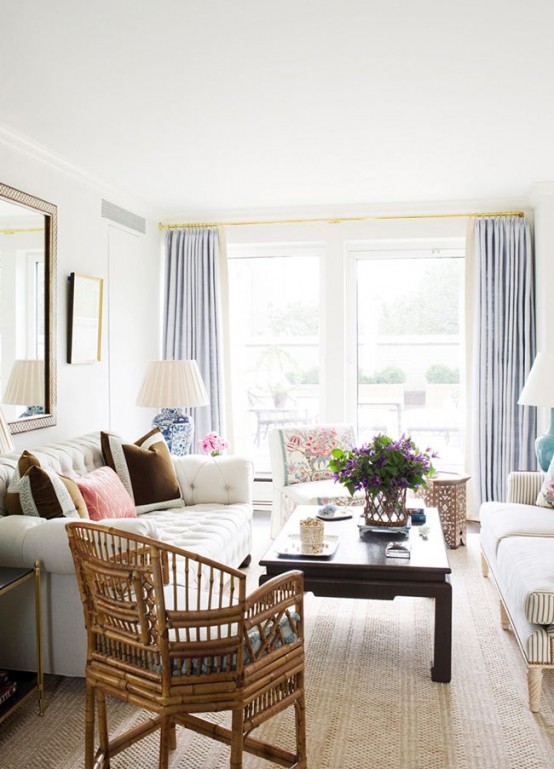 an eclectic living room with grey and creamy seating furniture, a dark coffee table, a rattan chair, light blue curtains and touches of gold