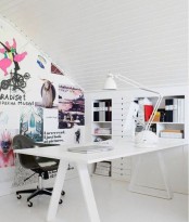a cool Nordic home office done in white, with built-in shelves and drawers, a trestle desk, a black chair and an accent wall with lots of fun art and decor