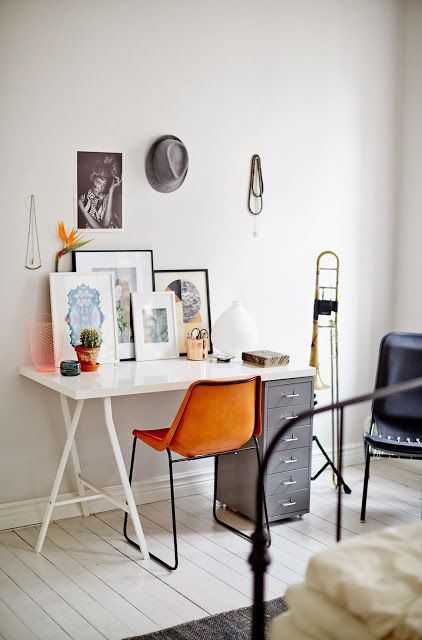 a Scandinavian home office with a white desk with a grey cabinet, an orange leather chair, a gallery wall and potted plants, some metal furniture