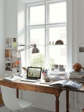 a Nordic home office with a vintage feel, a vintage wooden desk, a white chair, a table lamp, a glass shelf on the window and some memos on the wall