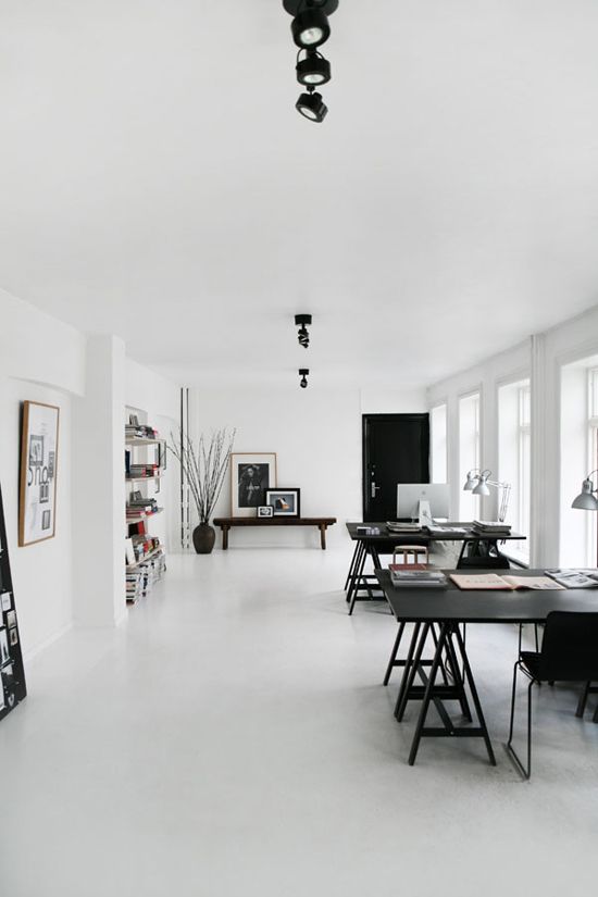 a large black and white Scandinavian home office with two large black desks and black chairs, a wooden bench, bookshelves and silver table lamps plus lots of natural light