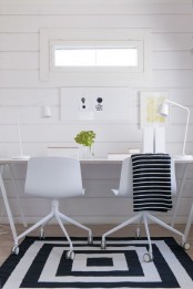 a lovely black and white Scandinavian home office with a white shared desk, white chairs, white table lamps and artwork