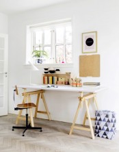 a neutral Scandinavian home office with a white and stained trestle desk, a plywood chair, a gallery wall and a box with various stuff