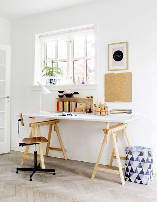 a neutral Scandinavian home office with a white and stained trestle desk, a plywood chair, a gallery wall and a box with various stuff