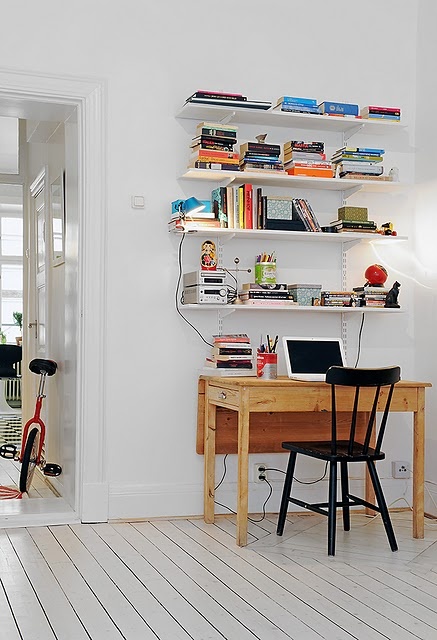 a small and pretty Scandinavian working nook with lots of wall-mounted bookshelves, a light-stained desk and a black chair is functional and cool