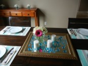 a simple centerpiece of a mirror, blue beads, candles and a colorful bloom centerpiece