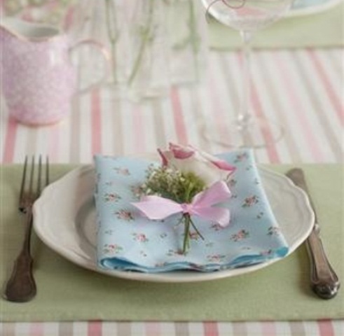 a simple pastel place setting with a floral napkin, a green placemat and a flower