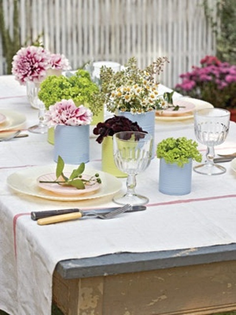 a pastel spring tablescape with pastel tin cans instead of vases and spring blooms, pastel plates and chargers