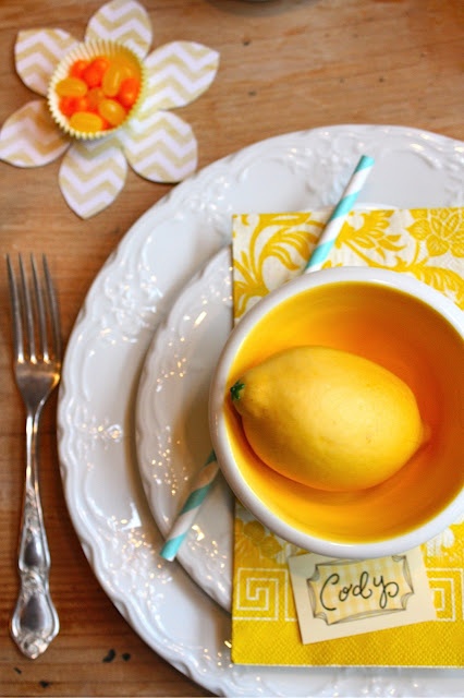 a chic place setting with white plates, a yellow napkin, a yellow bowl and a lemon