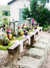 a spring table setting with a moss runner, colorful blooms and lanterns