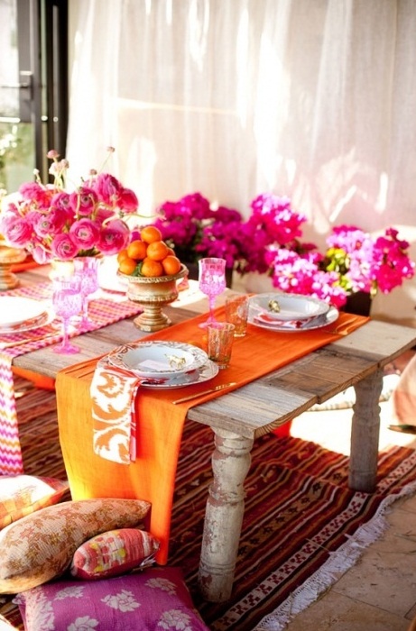 a super bright and colorful table setting in Moroccan style, with pink blooms, colorful napkins and runners and bright pillows