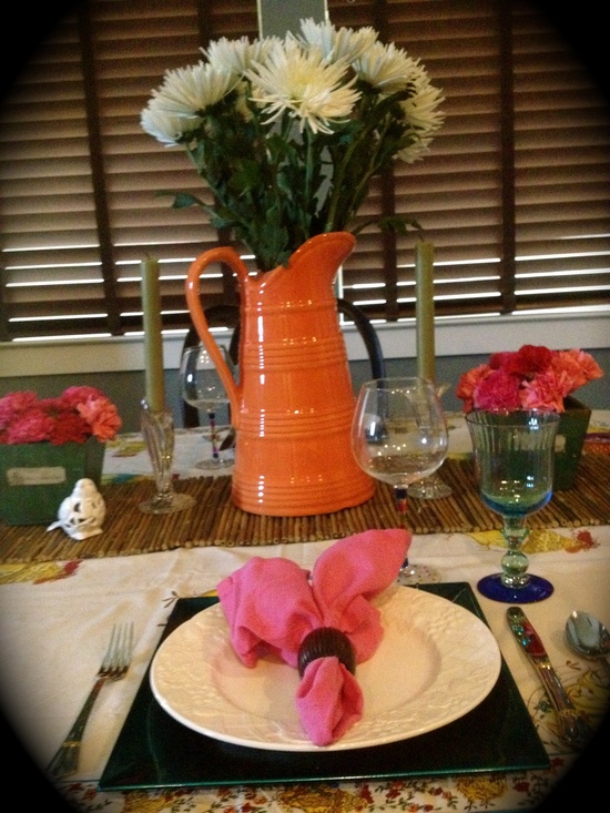 a colorful spring tablescape with a bright orange jug, pink napkins and blooms