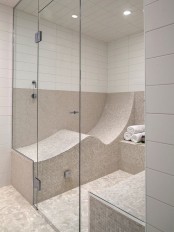 a stylish neutral steam room clad with small mosaic and white subway tiles, with curved benches clad in tiles that are very comfortable
