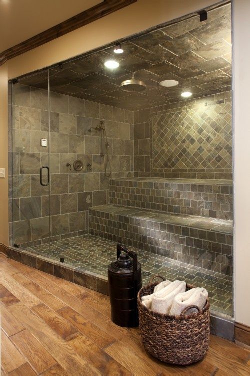 a large steam room clad with grey tiles in various patterns and with a single large bench plus a glass door is very cool