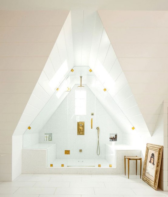 an attic white steam room with a window, two tile clad benches and gold fixtures looks airy and chic