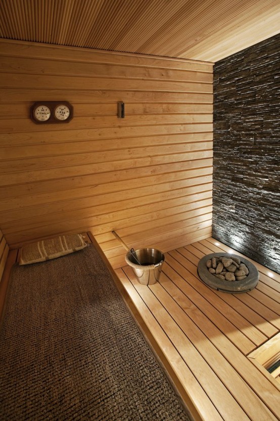 a cozy wood clad steam room with a stone wall and several benches, with a jute cover on one of them and some lights