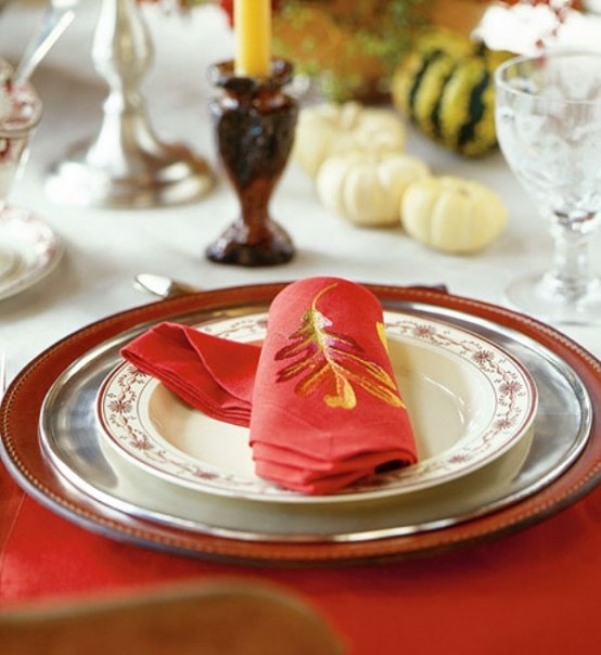 a red, silver and printed plate, a red napkin with an embroidered leaf for a chic and bright fall or Thanksgiving place setting with a modern feel