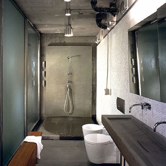 Several concrete walls provide industrial vibe to this bathroom but a light grey mosaic wall balances things out.