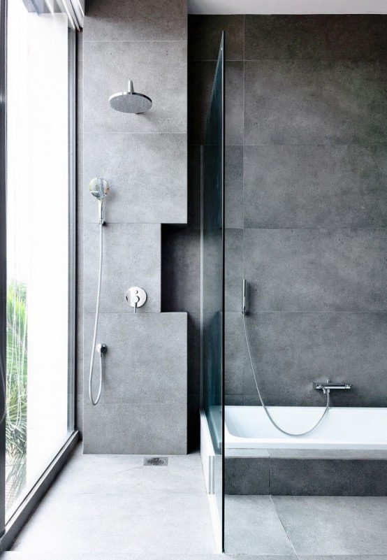 a contemporary fully concrete bathroom with a glazed wall and a bathtub clad with concrete tiles, too, is a bold and cool space