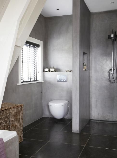 a minimalist bathroom with concrete walls, black tiles on the floor, a window and baskets for storage is cool