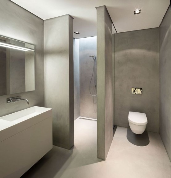 a minimalist and very sleek concrete bathroom with a mirror, a sleek white vanity and a sink, a shower space with a skylight