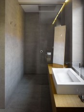 a minimalist concrete bathroom with a shower space separated from the bathroom with a glass divider and a sleek wooden vanity and a large sink