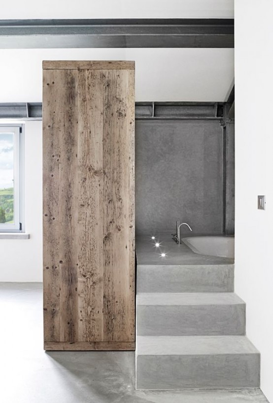 a concrete minimalist bathroom with concrete walls and a floor, a concete staircase and a built-in bathtub and a wooden dresser