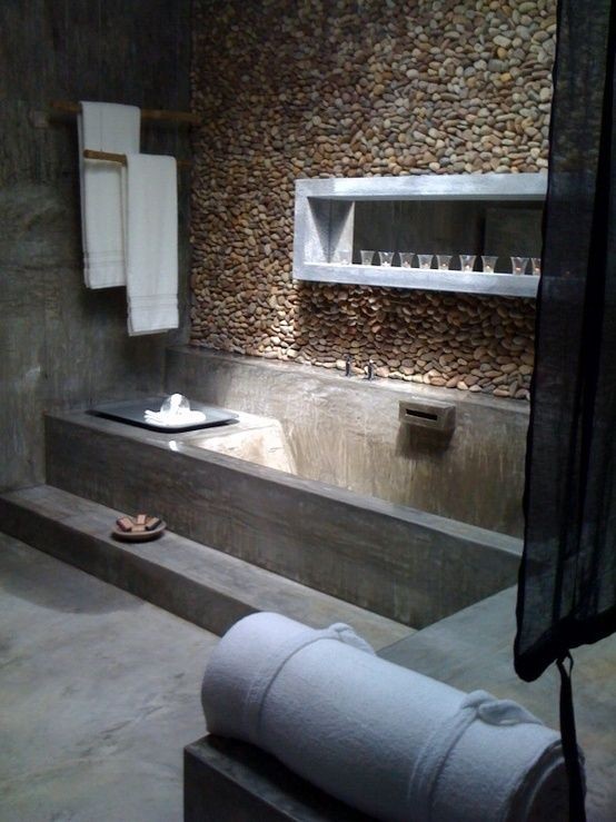 a wabi-sabi bathroom made of concrete, with a pebble wall, a built-in shelf and a bench, with neutral textiles is cool