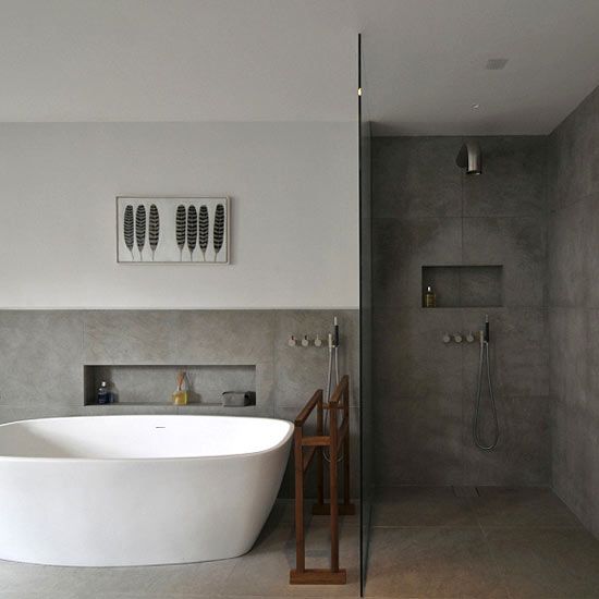 a minimalist bathroom clad with concrete tiles all over, a white bathtub, a wooden stand and simple modern fixtures