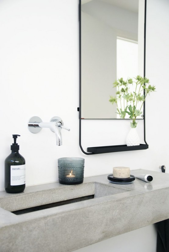a floating concrete vanity with a sink, a black mirror with a shelf, stylish fixtures and a candle is a chic space