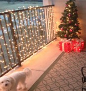 a balcony with a small Christmas tree with ornaments and lights and railing styled with lights are amazing for a festive feel