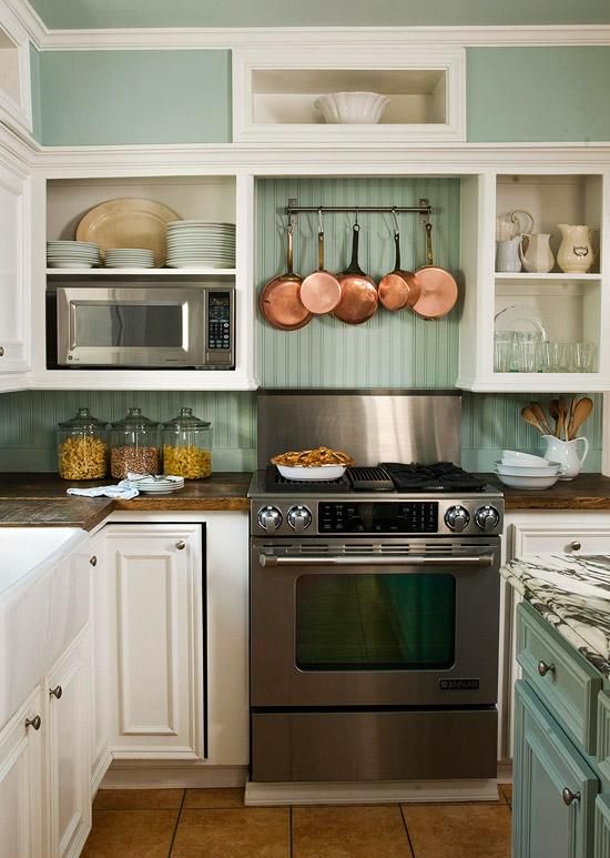 a cozy mint-colored and white cottage kitchen with open and closed storage units, a metal cooker and copper pans for decor is a very stylish space