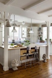 a white cottage kitchen with planked cabinets, lots of windows for natural light, pendant lamps and sconces and vintage urns with blooms