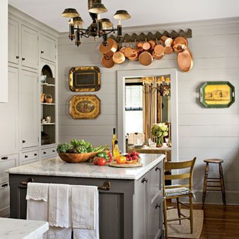 a stylish grey cottage kitchen with planked walls and vintage cabinets, a grey kitchen island with a stone countertop, copper pans and decorative trays for decor