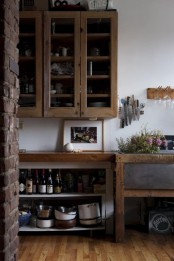 a rustic cottage kitchen with stained cabinetry, a metal sink in a wooden vanity, an exposed brick wall and artworks