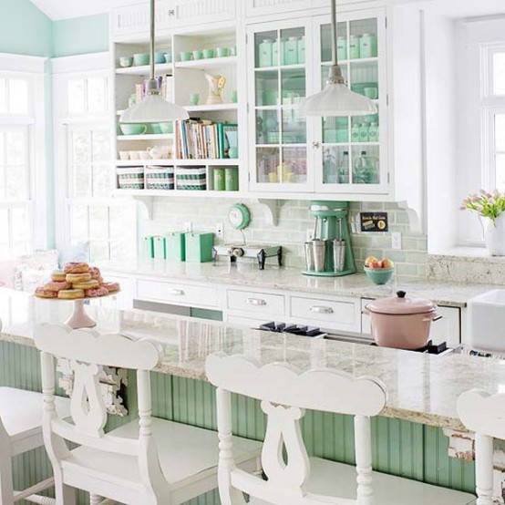 an airy and welcoming cottage kitchen with light green and white cabinets, tableware and cookware in greens, pendant lamps and vintage stools