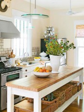 a charming cottage kitchen with a long table kitchen island, white cabinets with wooden knobs, pendant lamps and baskets plus bold blooms