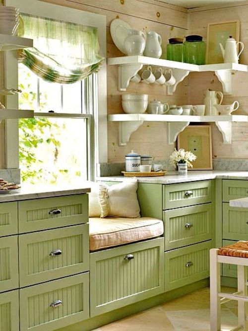 a cute green planked kitchen with open corner shelves, printed textiles and elegant vintage porcelain is a chic space