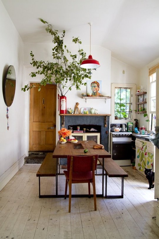 a cute cottage kitchen in neutrals with painted cabinets, a stained dining set, greenery branches in a red vase and a pendant lamp plus a round mirror