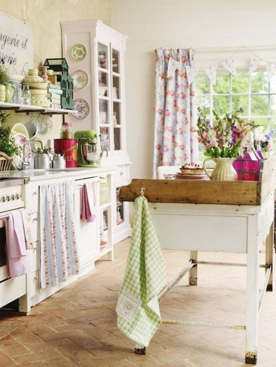 a lovely cottage kitchen with white cabinets, a white table kitchen island, colorful printed textiles and touches of green and pink