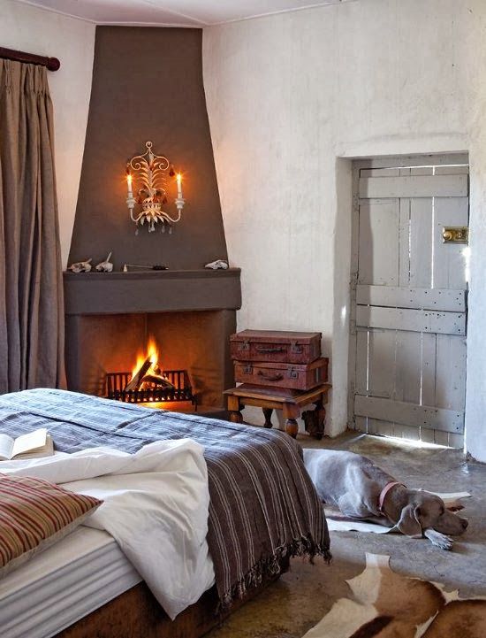 a quirky vintage bedroom with a dark firpelace in the corner, a bed with printed bedding, stacked vintage suitcases and cowhide rugs