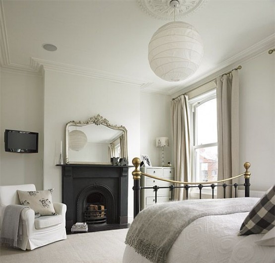 a neutral Parisian bedroom with a fireplace and a mirror, a metal bed with neutral bedding, a white chair and a pendant lamp plus a dresser in the corner