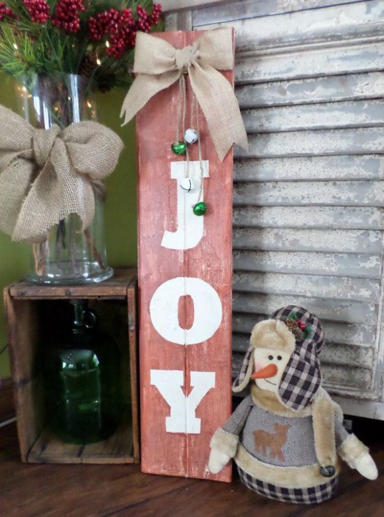 a rustic red Christmas sign with white letters, with white and grene bells and a burlap bow on top