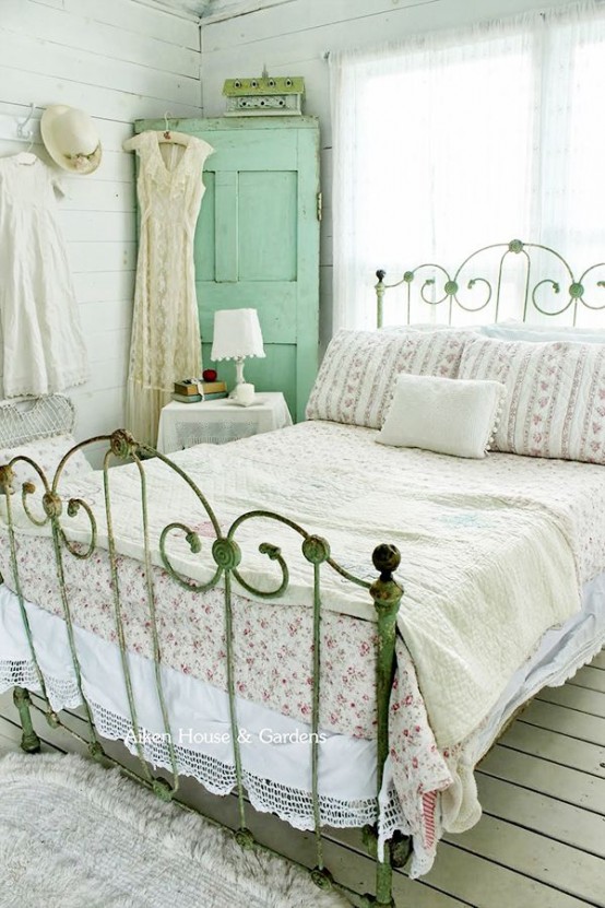 a neutral shabby chic bedroom with a simple wooden floors and walls, a forged bed, a mint storage unit, floral and lace bedding