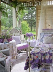 a colorful shabby chic bedroom done in lilac, purple and white, a forged bed, white wicker furniture, purple and lilac bedding and potted flowers
