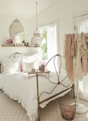 a neutral and pastel shabby chic bedroom with a forged bed, a refined mirror, a chic glass pendant lamp and an open closet with clothes on display