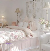 a neutral and pastel shabby chic bedroom with a forged screen instead of a headboard, white furniture, floral bedding and exquisite tall lamps